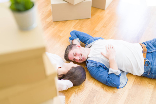 Young beautiful couple relaxing lying on the floor around cardboard boxes at home, smiling happy moving to a new house - Foto, Imagem