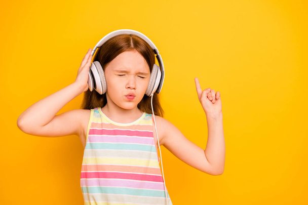Portrait of charming kid wearing tank-top singlet with closed eyes listening music isolated over yellow background - 写真・画像
