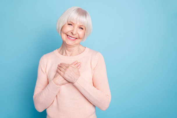 Portrait of positive woman putting her palm on chest smiling wearing pastel sweater isolated over blue background - Foto, imagen