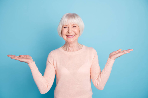 Portrait of pretty old woman holding hands with toothy smile wearing pastel jumper isolated over blue background - Photo, Image