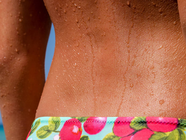 Menina bonita mostra suas costas finas bronzeadas ou coluna vertebral, ainda molhada com gotas de água de banho no oceano
. - Foto, Imagem