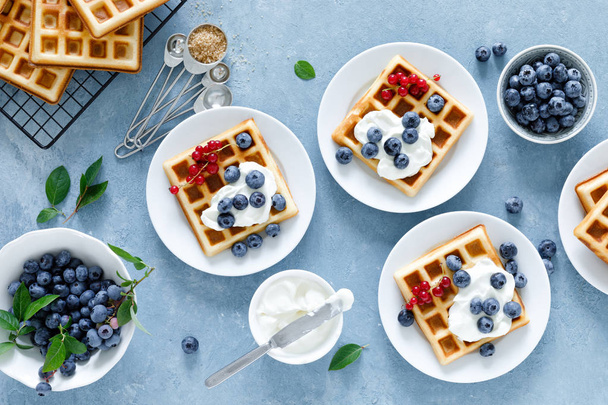 Traditional belgian waffles with cream cheese and fresh blueberry on blue background, top view - Foto, afbeelding