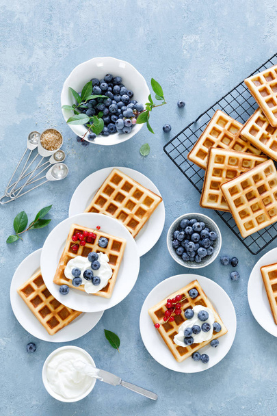 Traditional belgian waffles with cream cheese and fresh blueberry on blue background, top view - Фото, зображення