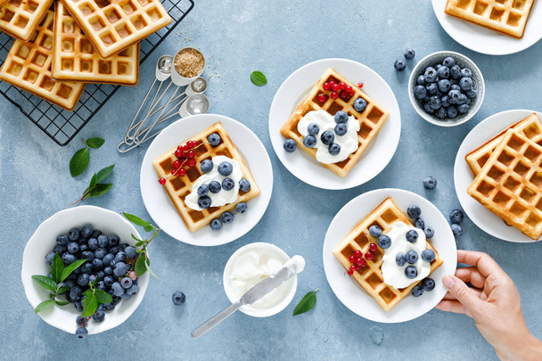 Traditional belgian waffles with cream cheese and fresh blueberry on blue background, top view - Fotó, kép