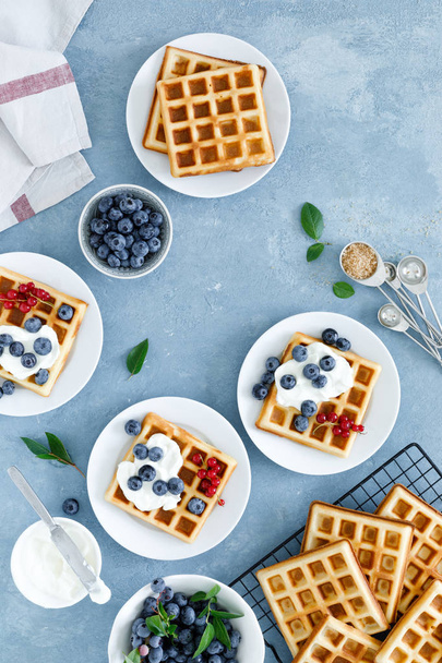 Traditional belgian waffles with cream cheese and fresh blueberry on blue background, top view - Foto, imagen
