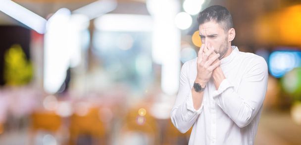 Young business man over isolated background smelling something stinky and disgusting, intolerable smell, holding breath with fingers on nose. Bad smells concept. - Photo, Image