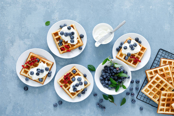 Traditional belgian waffles with cream cheese and fresh blueberry on blue background, top view - Foto, Bild