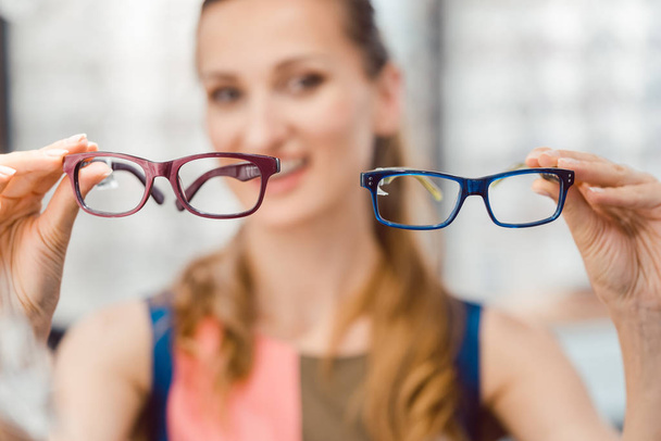 Vrouw kiezen tussen twee modellen van glazen bij optometrist - Foto, afbeelding