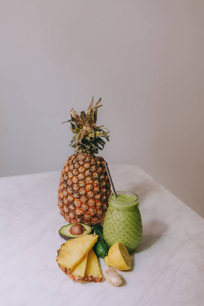 Homemade pineapple smoothie made with lemon, ginger, avocado, cucumber on a white table - Foto, afbeelding