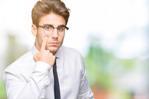 Jovem homem de negócios usando óculos sobre fundo isolado Apontando para o olho observando você gesto, expressão suspeita
 - Foto, Imagem