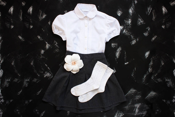 School uniform met wit overhemd, sokken en donkere denim rok op een zwarte achtergrond. Flatlay, bovenaanzicht, kopieer ruimte. - Foto, afbeelding