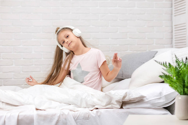 little girl listening to the music with the headphones on bed. - Photo, Image