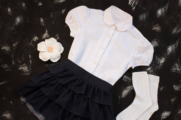 Uniforme escolar con camisa blanca, calcetines y falda de mezclilla oscura sobre fondo negro. Flatlay, vista superior, espacio para copiar
. - Foto, imagen