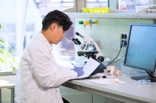 Asian scientist working in lab. Doctor making microbiology research. Laboratory tools: microscope, test tubes, equipment. Biotechnology, chemistry, bacteriology, virology, dna and health care. - Photo, image