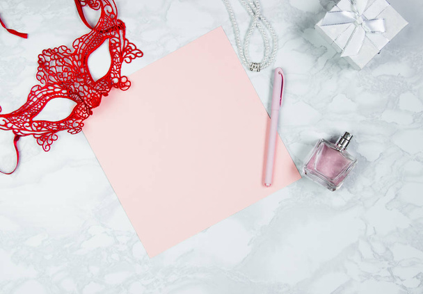 Women's accessories on a white marble table. A pink sheet of paper, a pink pen, a perfume, a gift box, pearls, a glass of coffee and a circling red mask. Layout for adding tags. Top view, flat lay, co - Foto, Bild