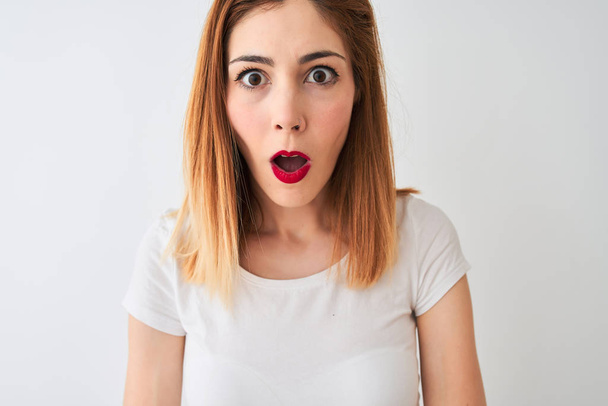 Beautiful redhead woman wearing casual t-shirt standing over isolated white background scared in shock with a surprise face, afraid and excited with fear expression - Fotografie, Obrázek