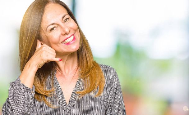 Beautiful middle age business woman smiling doing phone gesture with hand and fingers like talking on the telephone. Communicating concepts. - 写真・画像