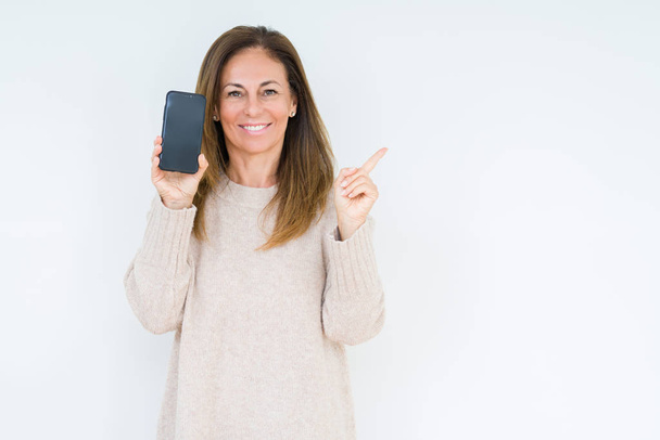 Középkorú nő mutatja smartphone képernyőn át elszigetelt háttér nagyon boldog mutatva kéz és az ujját az oldalsó - Fotó, kép