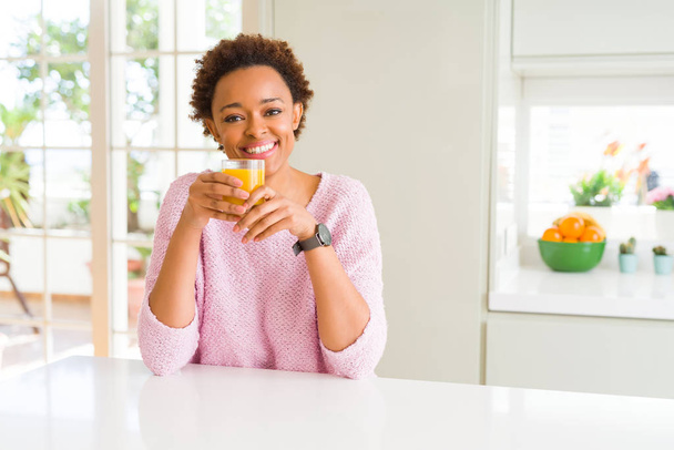Nuori afrikkalainen amerikkalainen nainen driking appelsiinimehua kotona onnellinen kasvot seisoo ja hymyilee luottavainen hymy osoittaa hampaat
 - Valokuva, kuva