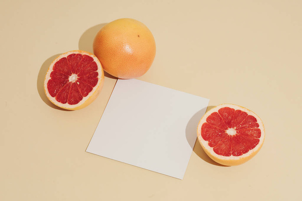 Minimal sunlit fruit composition of grapefruits with shadows and white paper card note on sandy color background. Summer creative concept  - Fotografie, Obrázek
