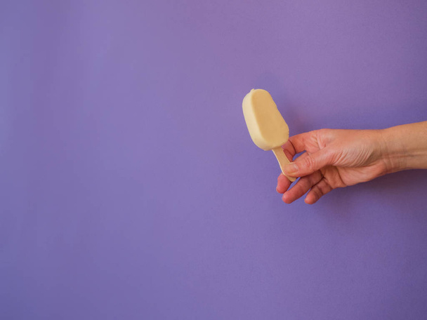 Hand with white chocolate lollipop icecream on purple background - Фото, зображення