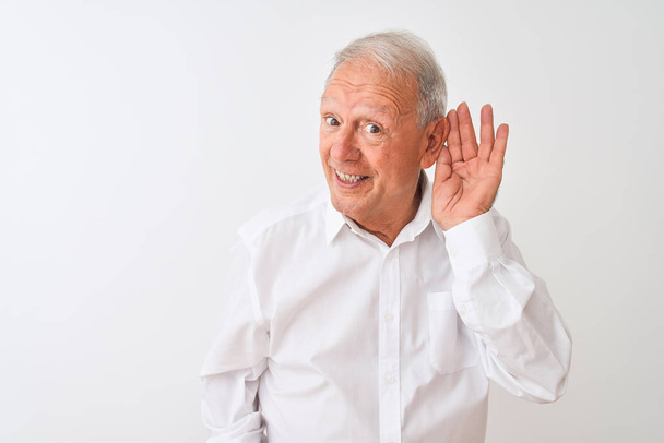 Senior grey-haired man wearing elegant shirt standing over isolated white background smiling with hand over ear listening an hearing to rumor or gossip. Deafness concept. - Foto, immagini