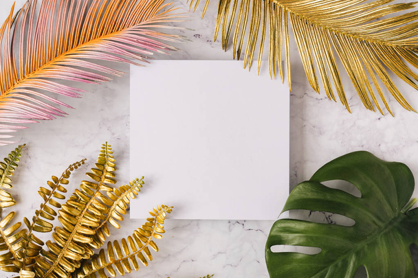 Beyaz mermer arka plan üzerinde beyaz kağıt kart notu ile altın ve renkli tropikal palmiye yapraklarından yapılmış yaratıcı düzen. Minimal yaratıcı yaz konsepti  - Fotoğraf, Görsel