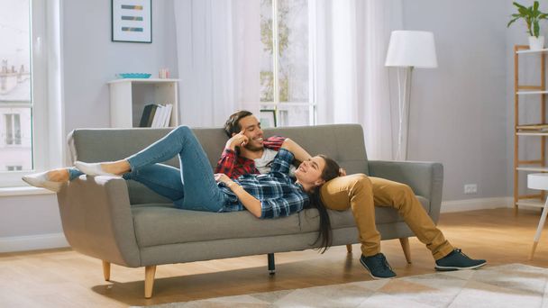 Mutlu genç çift oturma odasında yeni bir kanepede yatıyor ve dinlenmek zorunda. Parlak modern daire-şık mobilyalarla. - Fotoğraf, Görsel