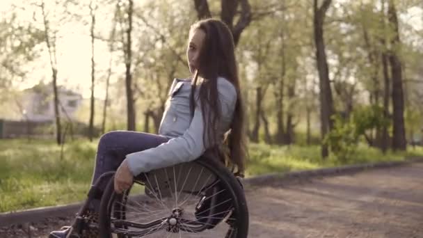 Νεαρά όμορφη ανάπηρος γυναίκα σε αναπηρικό αμαξίδιο περπατώντας στο πάρκο το βράδυ - Πλάνα, βίντεο