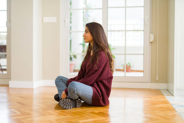 Mladá krásná žena sedí na podlaze doma při pohledu na stranu, uvolnit profilu pozice s přirozenou tvář s sebejistý úsměv. - Fotografie, Obrázek
