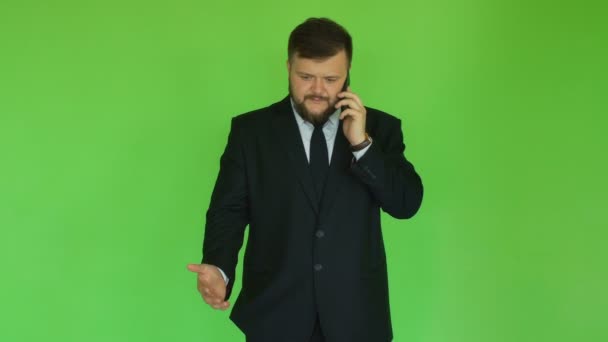 Angry businessman talks and shouts to phone, dissatisfied with the interlocutor. Chromakey Green. Bearded thick guy in black suit solves problems by smartphone. Man discusses important issues - Кадры, видео
