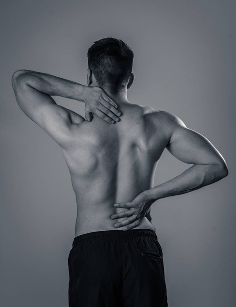 Young muscular fitness man touching and grabbing his neck and lower back suffering cervical pain isolated on neutral background. In sport and workout injury, Incorrect posture problems and body care. - Photo, image