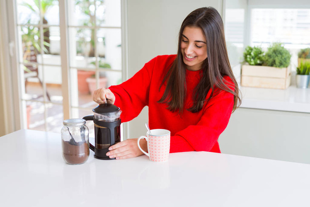 Joven hermosa mujer haciendo café de la mañana sonriendo, preparando una taza de café con leche para el desayuno
 - Foto, imagen