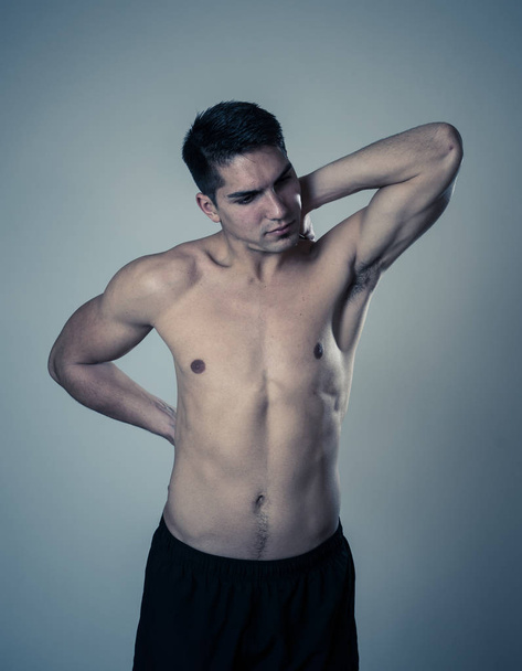 Young muscular fitness man touching and grabbing his neck and lower back suffering cervical pain isolated on neutral background. In sport and workout injury, Incorrect posture problems and body care. - Foto, Imagem