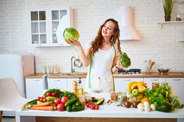 Молодая счастливая женщина держит брокколи и капусту на красивой кухне с зелеными свежими ингредиентами в помещении. Концепция здорового питания и диеты. Потеря веса
 - Фото, изображение