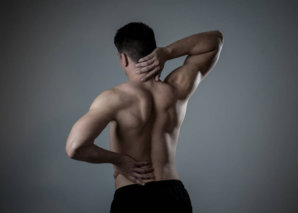 Young muscular fitness man touching and grabbing his neck and lower back suffering cervical pain isolated on neutral background. In sport and workout injury, Incorrect posture problems and body care. - Photo, image
