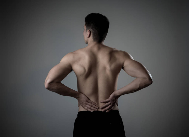 Young muscular fitness man touching and grabbing his lower back suffering strong pain after workout. Isolated on neutral background. In sport injury Incorrect posture problems and body health care. - Fotografie, Obrázek