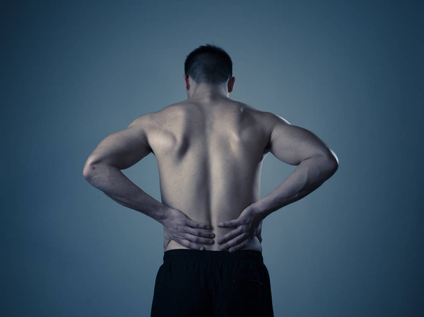 Young muscular fitness man touching and grabbing his lower back suffering strong pain after workout. Isolated on neutral background. In sport injury Incorrect posture problems and body health care. - Photo, image