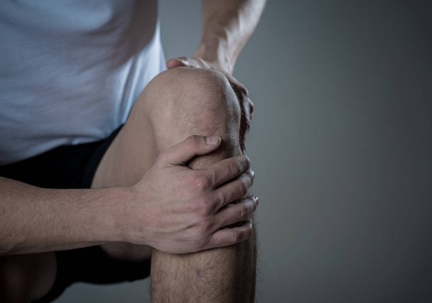 Young fit man holding knee with hands in pain after suffering muscle injury broken bone leg pain sprain or cramp during running workout. In Body pain and sport training injury and body health care. - Valokuva, kuva