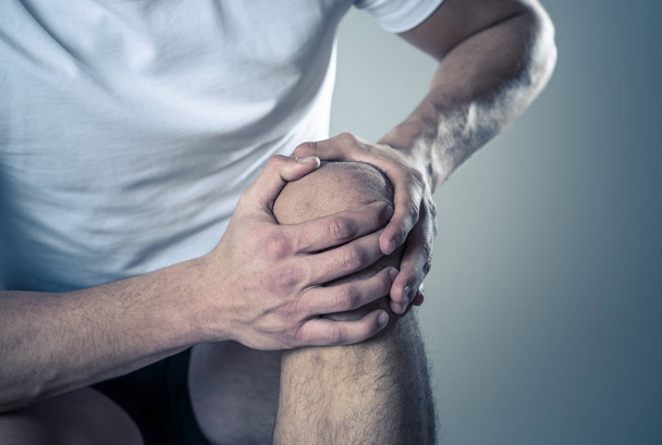 Молодой человек, держащий колено с болью в руках после травмы мышцы, сломанной боли в ноге или судороги во время тренировки. В боли в теле и спортивной подготовки травмы и здравоохранения тела
. - Фото, изображение