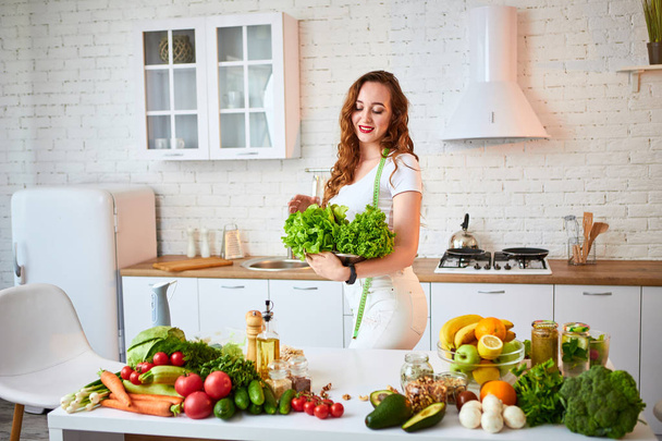 Joven mujer feliz sosteniendo hojas de lechuga para hacer ensalada en la hermosa cocina con ingredientes frescos verdes en el interior. Comida saludable y concepto de dieta. Perder peso
 - Foto, imagen