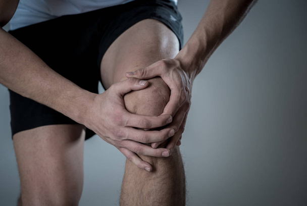 Young fit man holding knee with hands in pain after suffering muscle injury broken bone leg pain sprain or cramp during running workout. In Body pain and sport training injury and body health care. - Fotó, kép