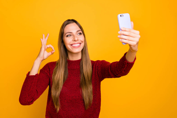 Pretty lady holding telephone hands making selfies showing okey symbol wear knitted pullover isolated yellow background - Foto, Imagem