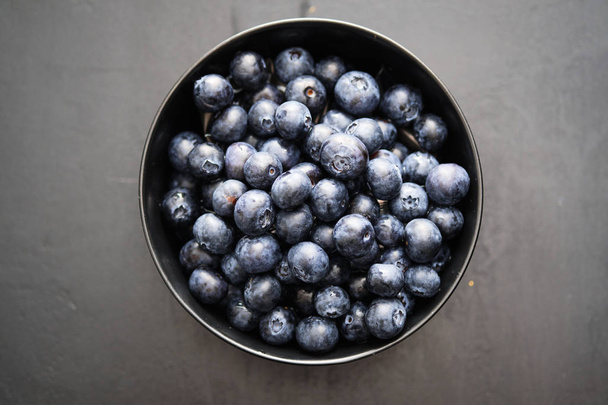Top view of freshly picked blueberries in black bowl on dark background - Foto, Imagem