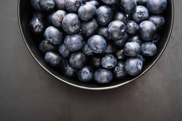 Top view of freshly picked blueberries in black bowl on dark background - Foto, Imagen