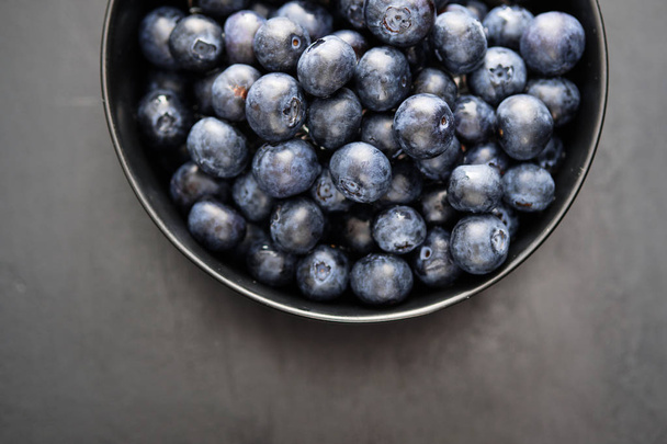 Top view of freshly picked blueberries in black bowl on dark background - Foto, Imagem