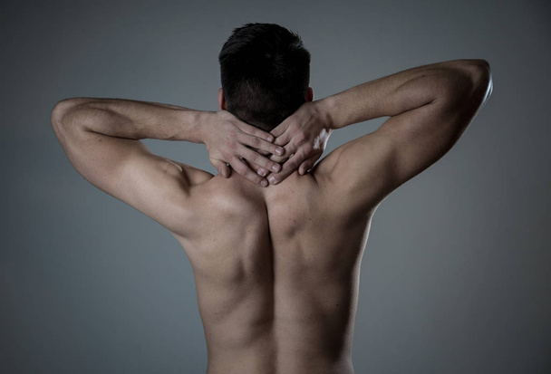 Young muscular fit man touching and grabbing neck and upper back suffering cervical pain after workout. Isolated on neutral background. In sport injury Incorrect posture problems and body health care. - Foto, immagini