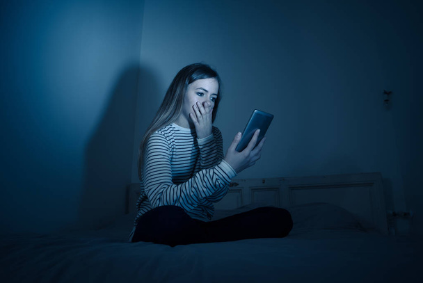 Sad desperate young teenager female girl on smart phone suffering from online bulling and harassment felling lonely and hopeless sitting on bed at night. CYberbullying and dangers of internet concept. - Photo, image