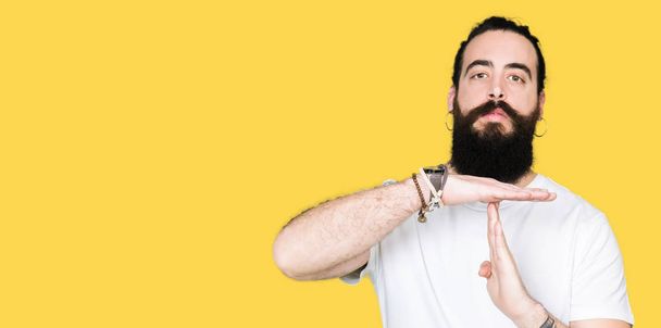 Young hipster man with long hair and beard wearing casual white t-shirt Doing time out gesture with hands, frustrated and serious face - Foto, Bild