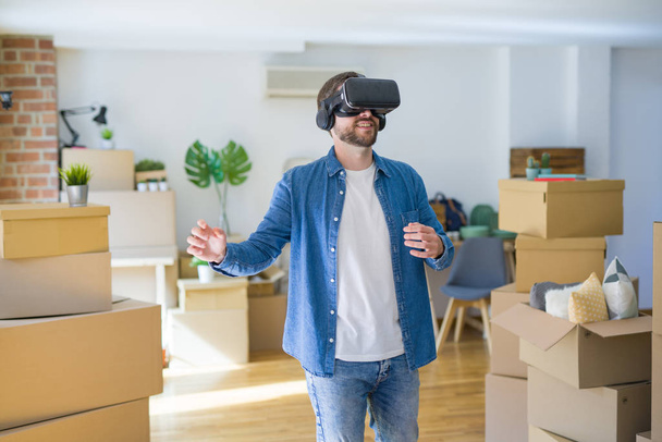 Nuori mies yllään virtuaalitodellisuus lasit pelaa simulointi peli ympäri pahvilaatikoita siirtymässä uuteen taloon
 - Valokuva, kuva